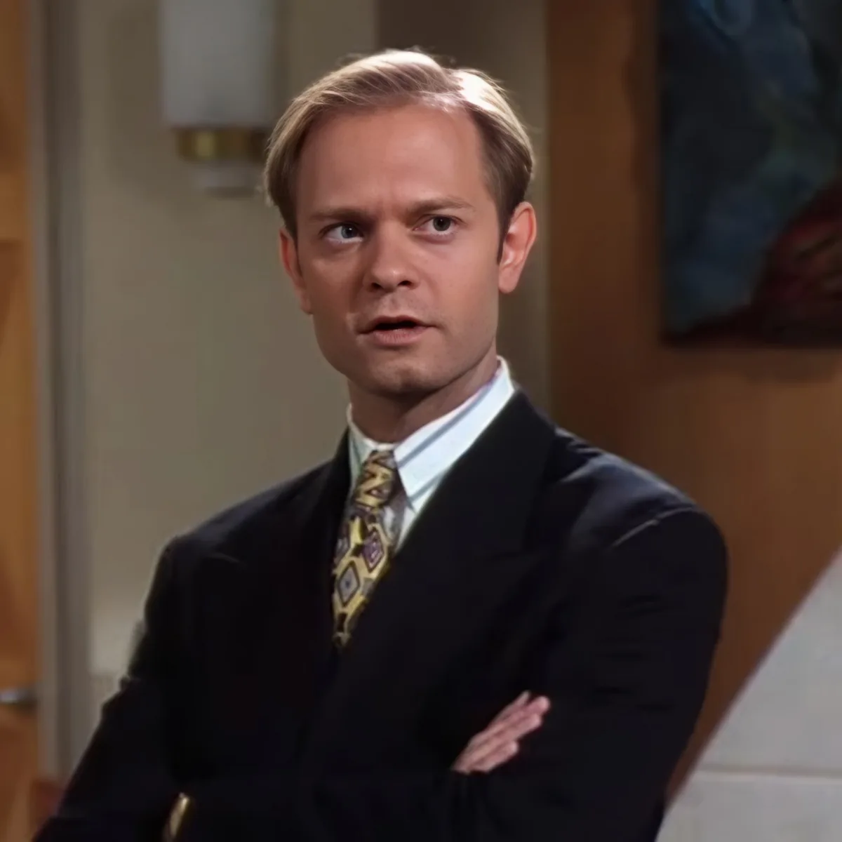 A man in a suit and tie with his arms crossed, looking surprised or concerned.