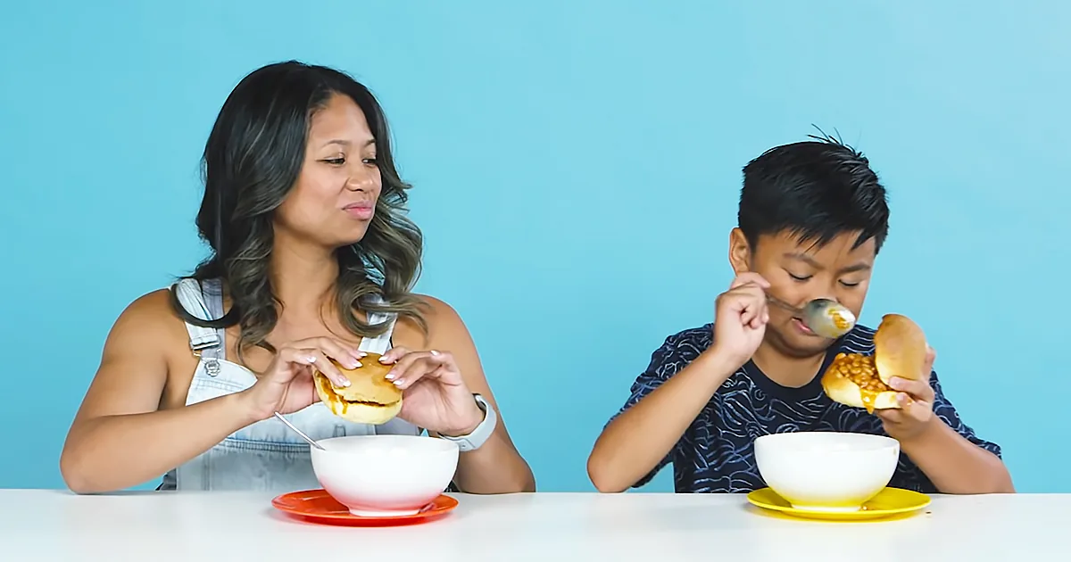 A woman and a boy are eating sandwiches with bowls of soup in front of them.