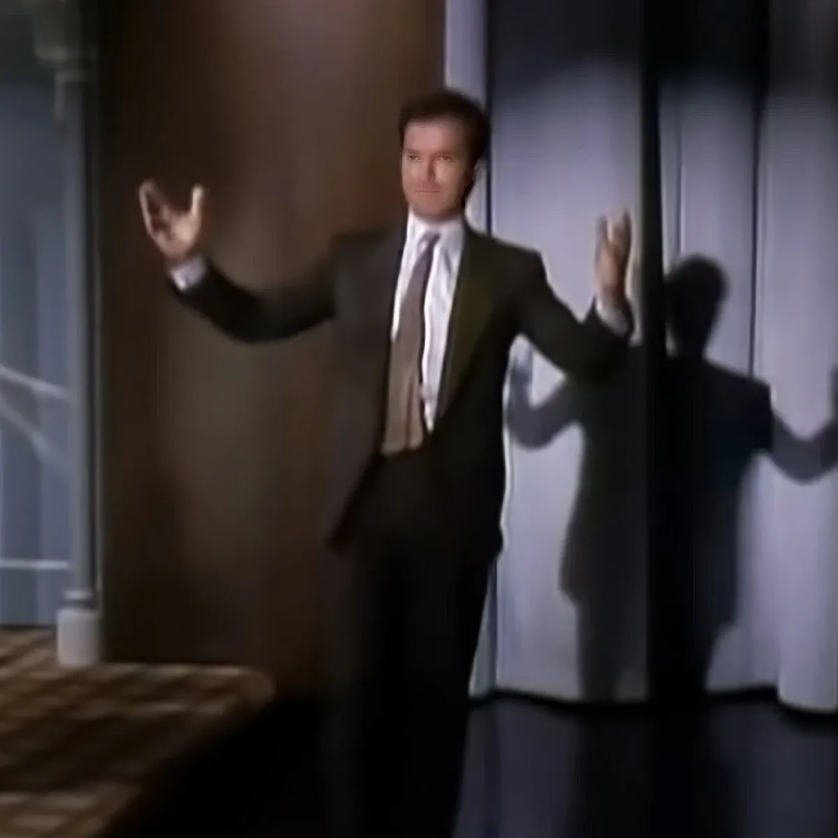 A man in a suit raises his arms, casting a shadow on a wall.
