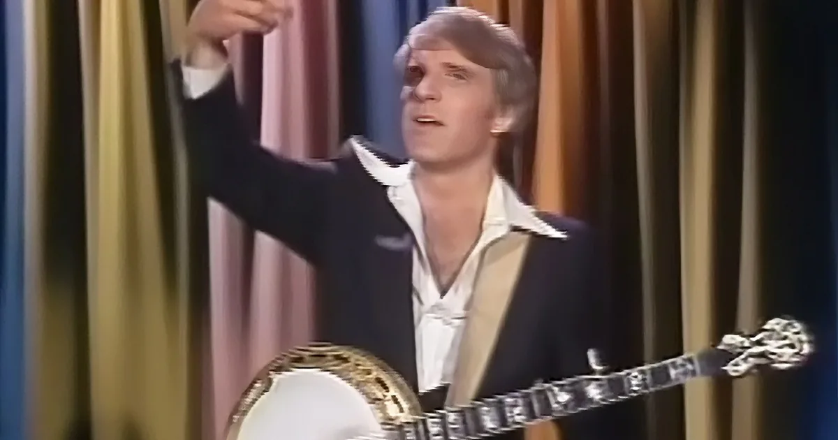 A person in a suit holds a banjo, raising their arm, against a striped backdrop.