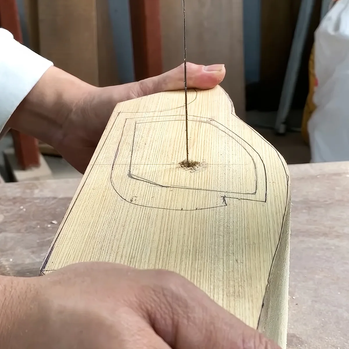 A person is using a tool to cut along a marked outline on a piece of wood.