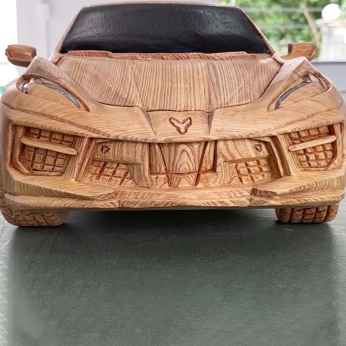 A wooden model of a sports car with intricate details and a glossy finish is displayed on a dark surface.