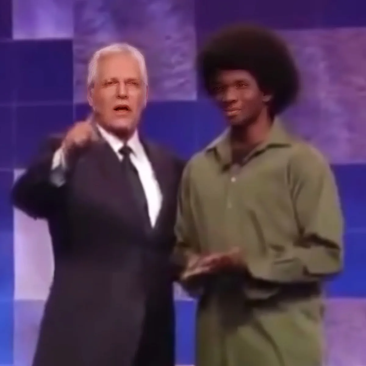 A man in a suit and tie is being embraced by another man in a green shirt on a stage.