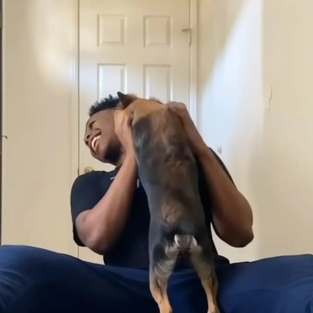 A man in a dark shirt is playfully lifting a small dog with a brown and black coat.