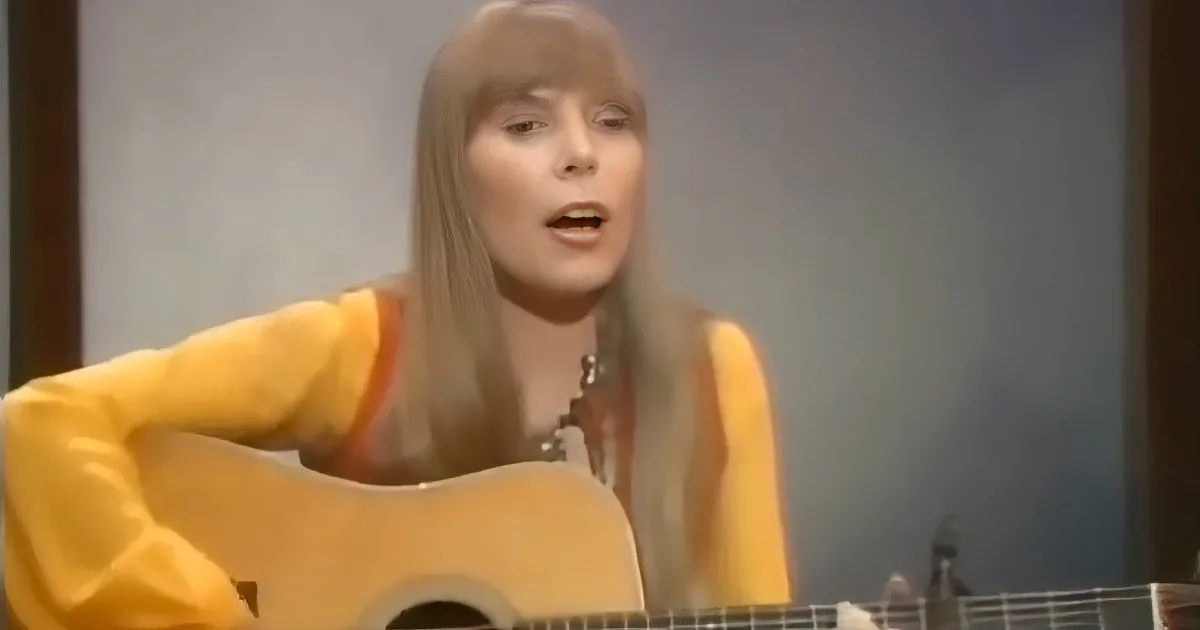 A woman in a yellow outfit sings while playing a guitar.