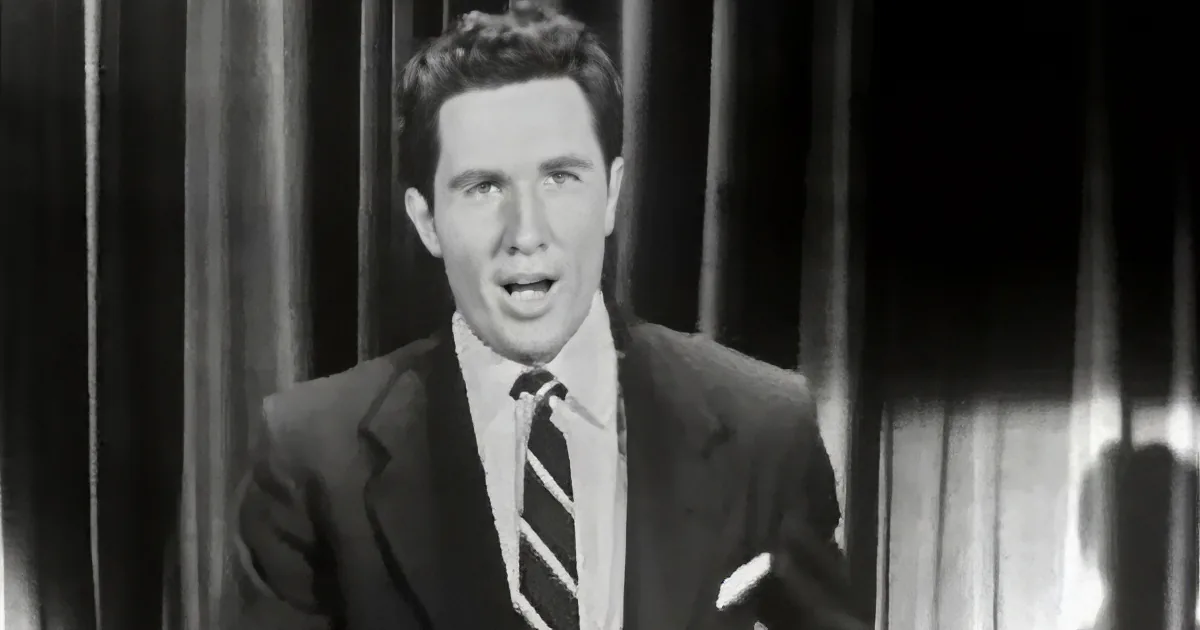 A man in a suit and tie is speaking into a microphone, appearing to be on a television show.