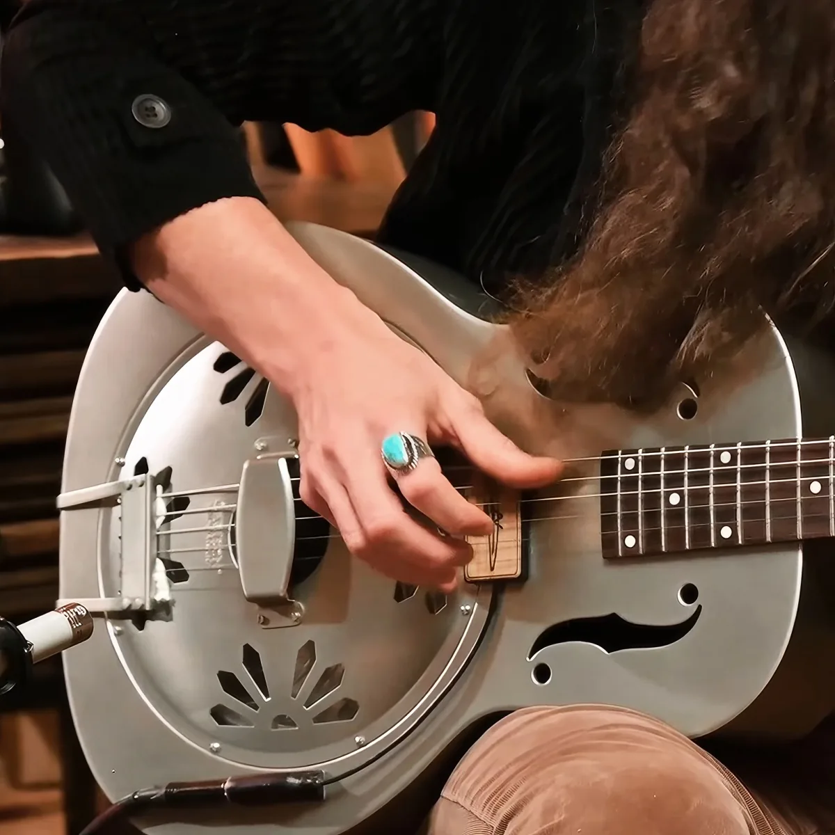A person plays a resonator guitar, focusing on the neck and hand position.