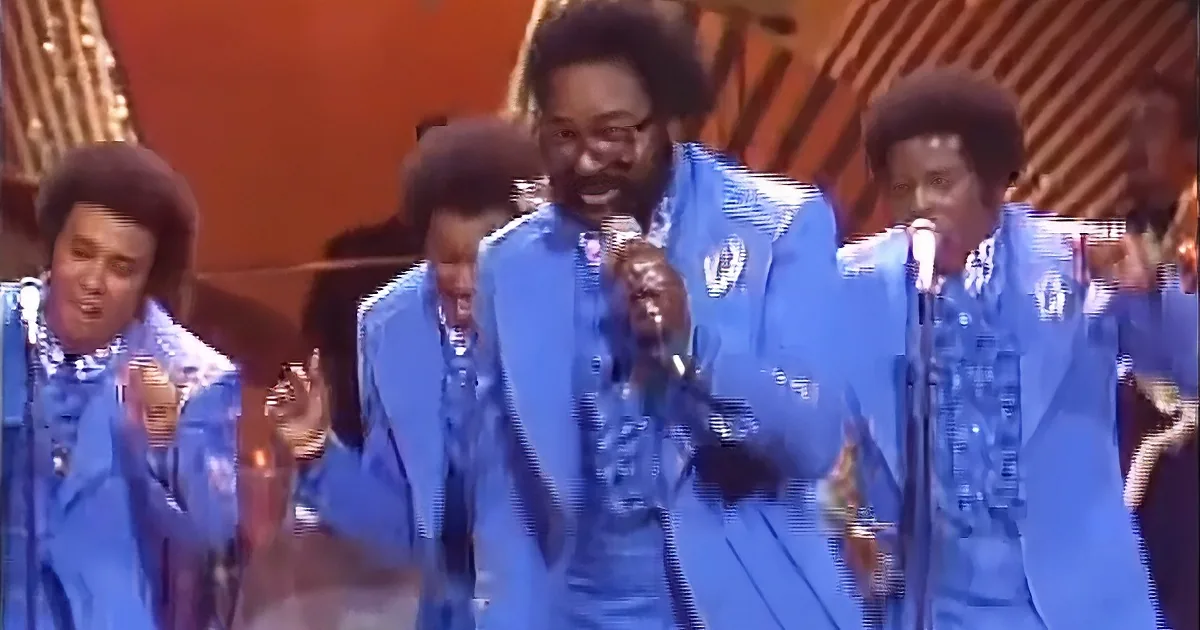A group of men in blue suits sing into microphones on stage.