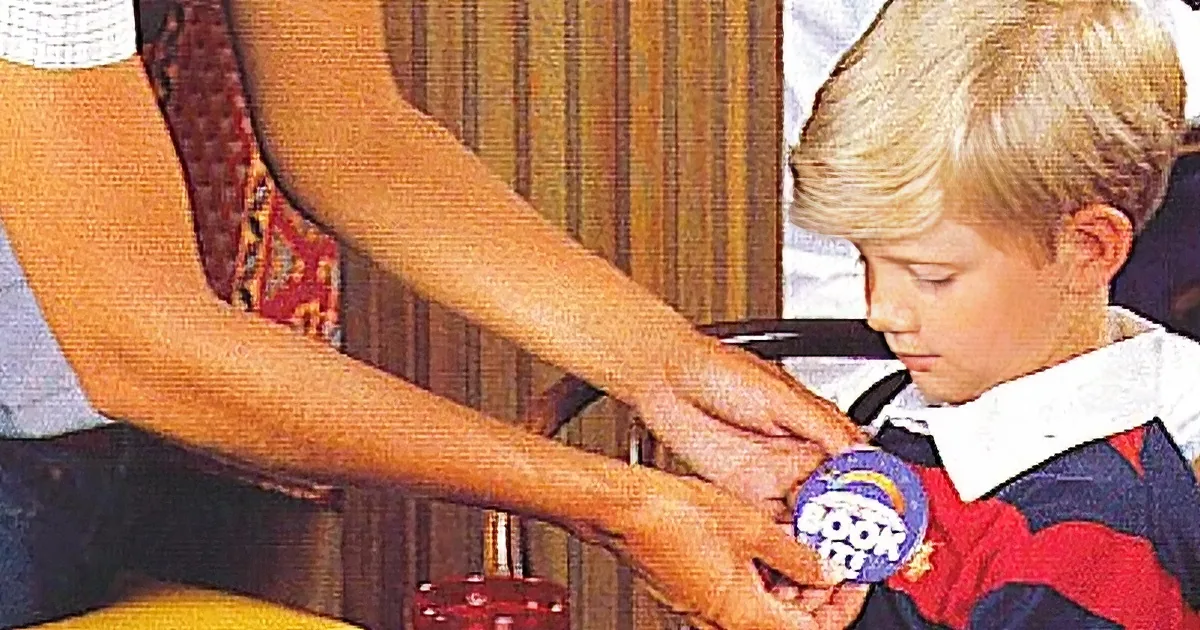 A young boy receives a badge from an adult's hands, with a striped background.