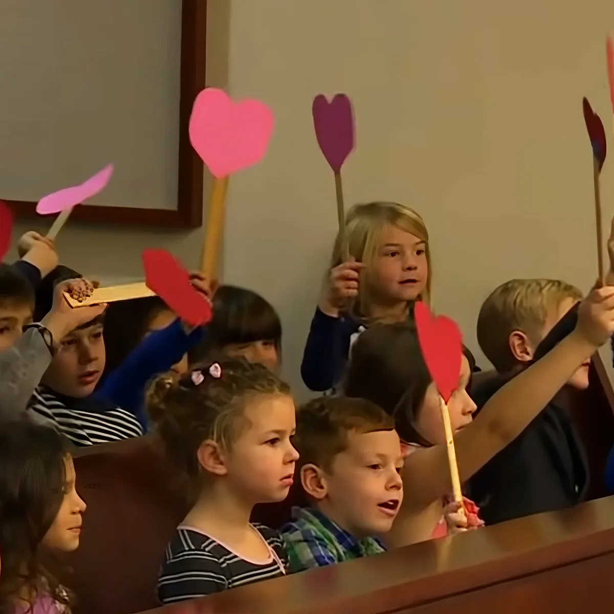 Children hold heart-shaped signs, likely participating in a classroom activity or celebration.