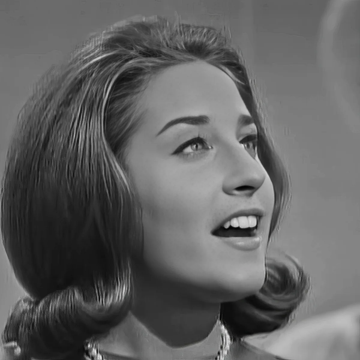 A woman with shoulder-length hair and a necklace, looking upwards with a slightly open mouth.