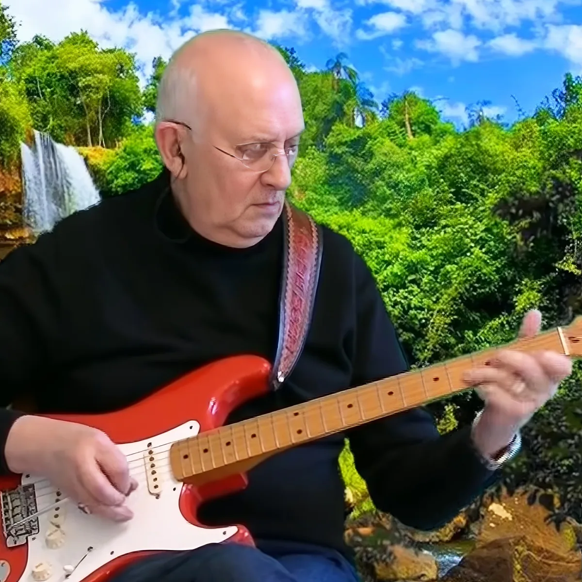 A man in a black shirt plays a red electric guitar against a lush green backdrop with a waterfall.