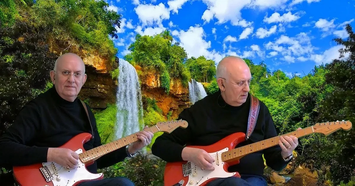 An older man plays a red electric guitar with a scenic waterfall and lush greenery in the background.
