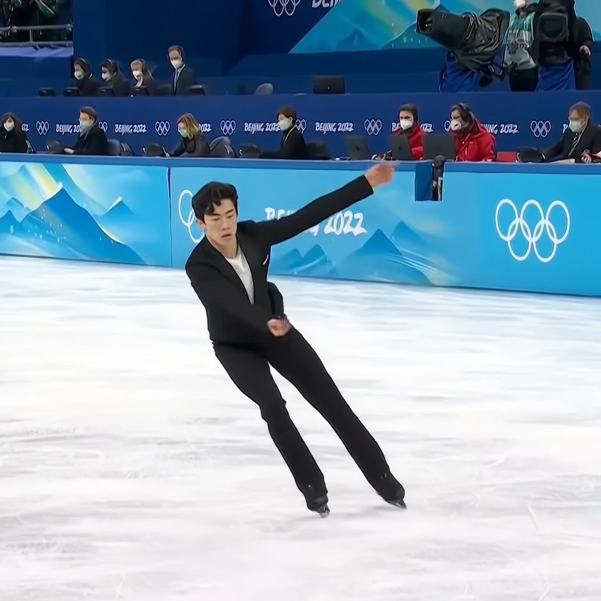A figure skater in black attire glides gracefully on ice, arms outstretched, against a backdrop of the Beijing 2022 Olympics.