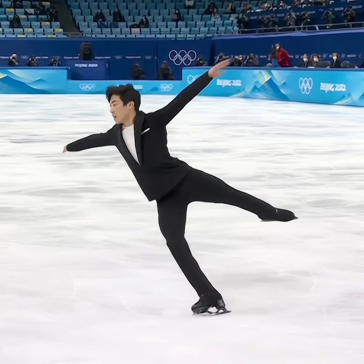 A figure skater in a black outfit performs a graceful pose on the ice.