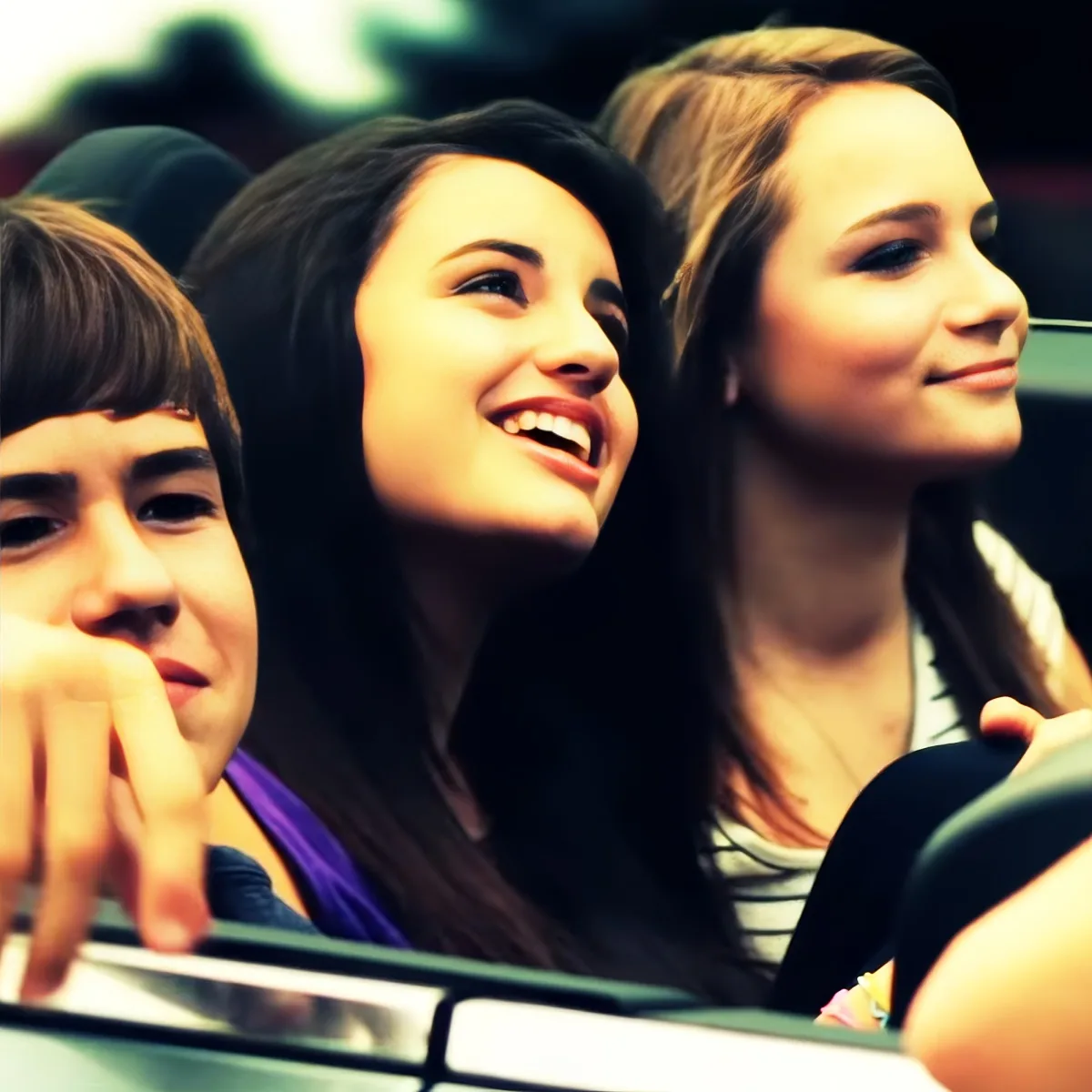 Three people, two women and a man, are smiling and looking up, possibly at a performance or event.