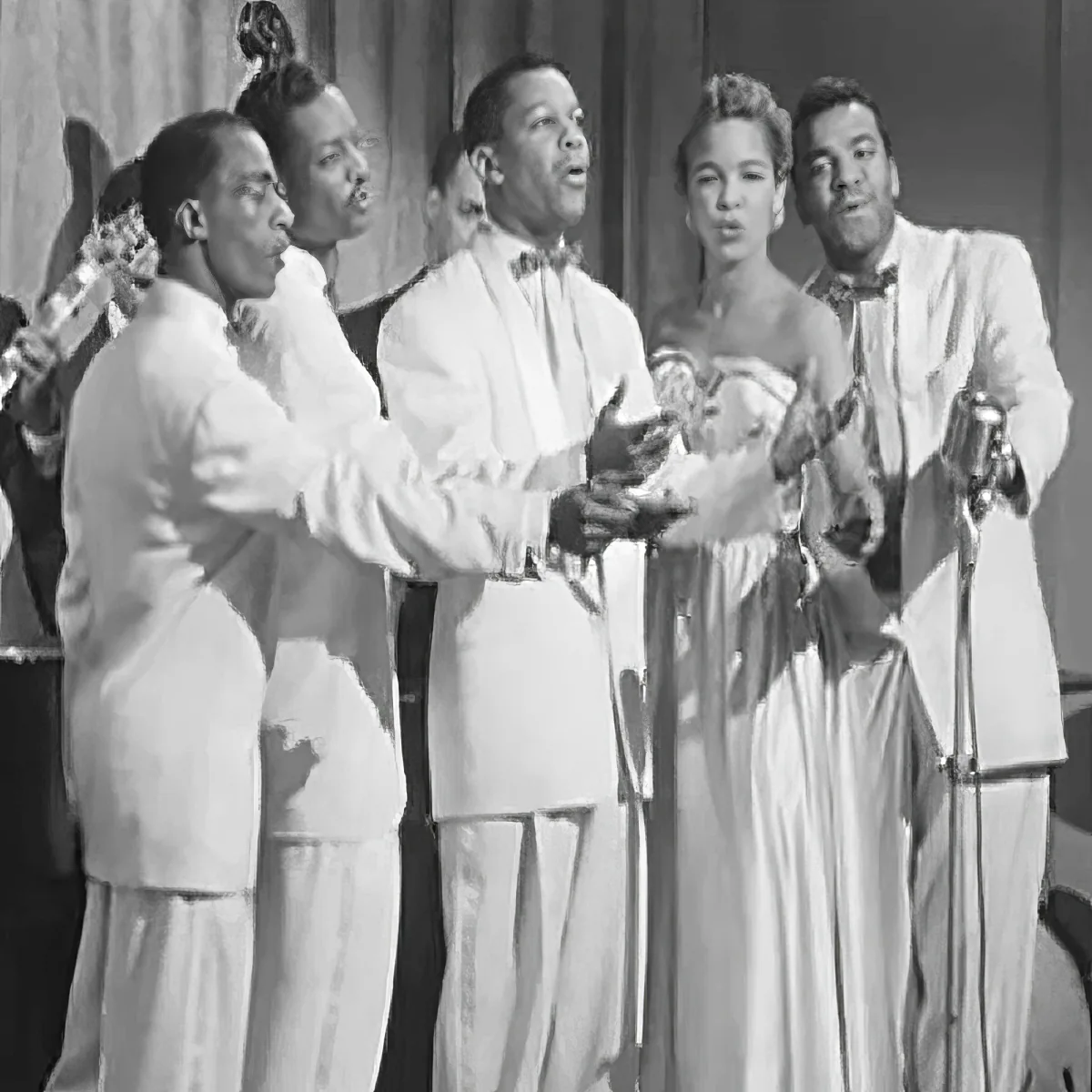 A group of performers in white outfits sing and gesture on stage, with microphones and a curtain backdrop.