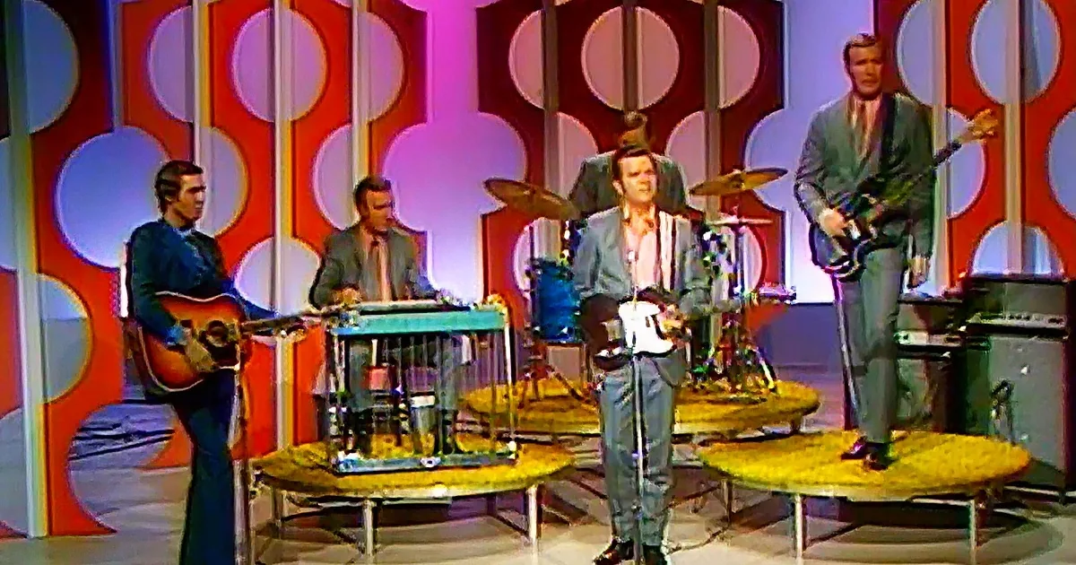 A band performs on a stage with a colorful, retro background, featuring a guitarist, keyboardist, drummer, and bassist.