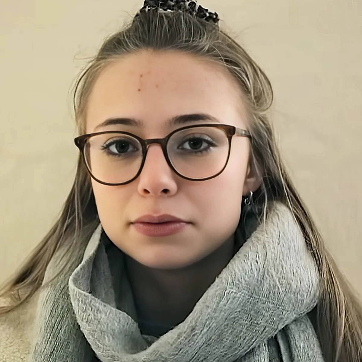 A person with glasses, light skin, and a grey scarf, looking directly at the camera.