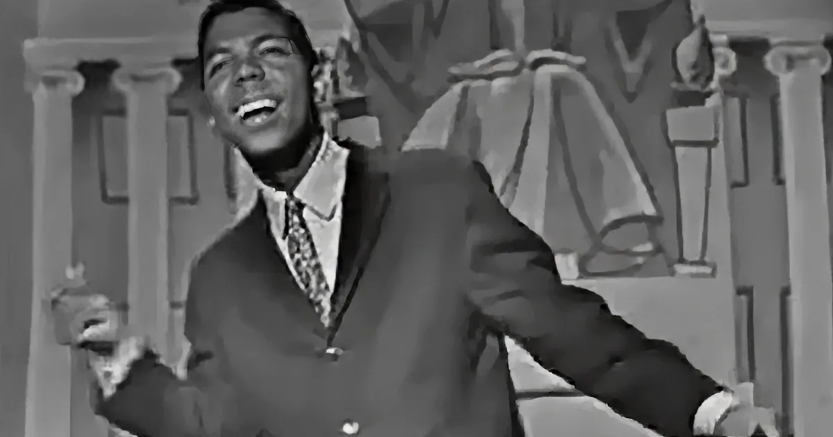A man in a suit and tie is smiling and gesturing with his hands.