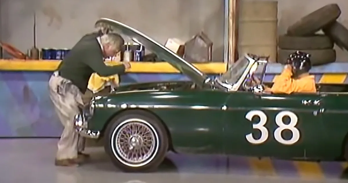 A man in a green shirt works on a vintage green car with the number 38 on its side.