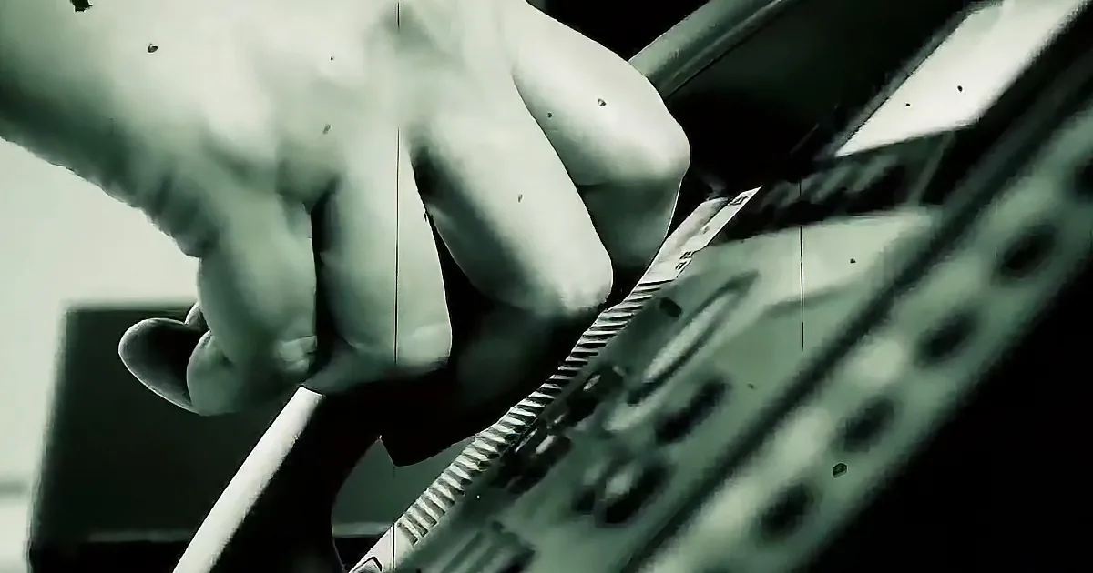 A hand is gripping a textured object, possibly a guitar neck, with a blurred background.