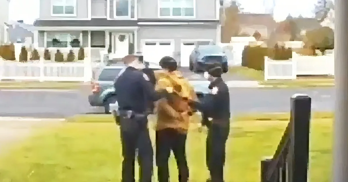 A person is being restrained by two police officers in a residential area.