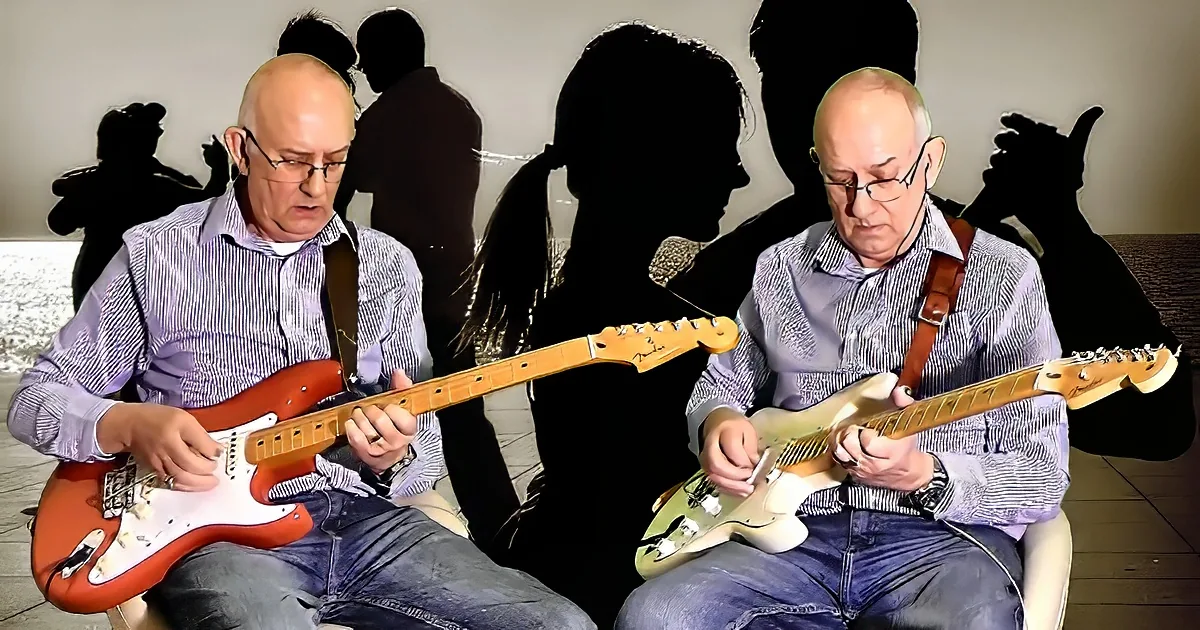 Two men play guitars, one red, one white, in a dimly lit room with silhouettes of people in the background.