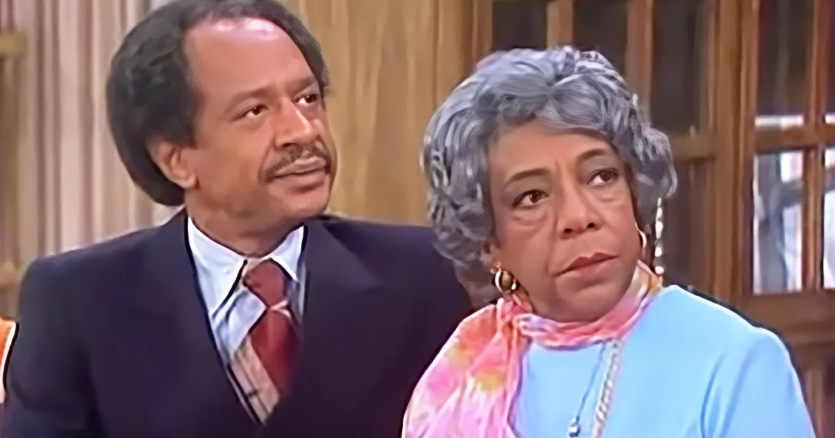 A man in a suit and tie sits beside a woman with gray hair, both looking off to the side.