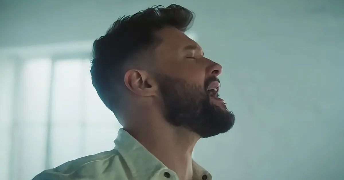 A man with a beard and short hair, wearing a light green shirt, looks upwards with his eyes closed.
