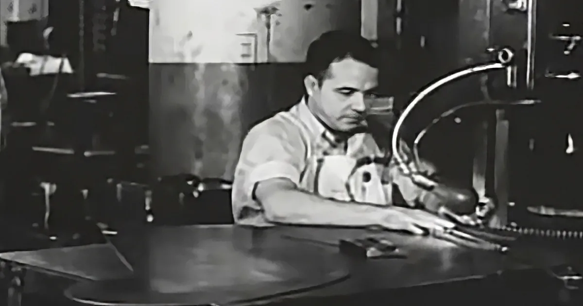A man in a workshop setting, focused on a task involving a tool and a piece of metal.