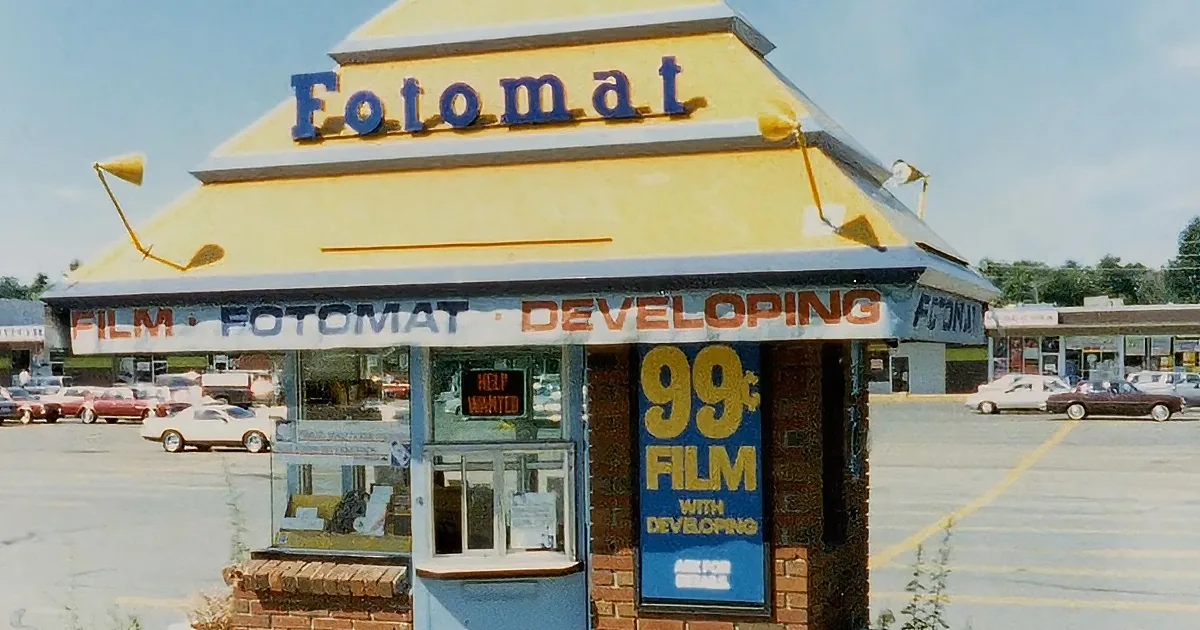 A Fotomat store with a yellow sign and "99¢ Film with Developing" sign in a parking lot.