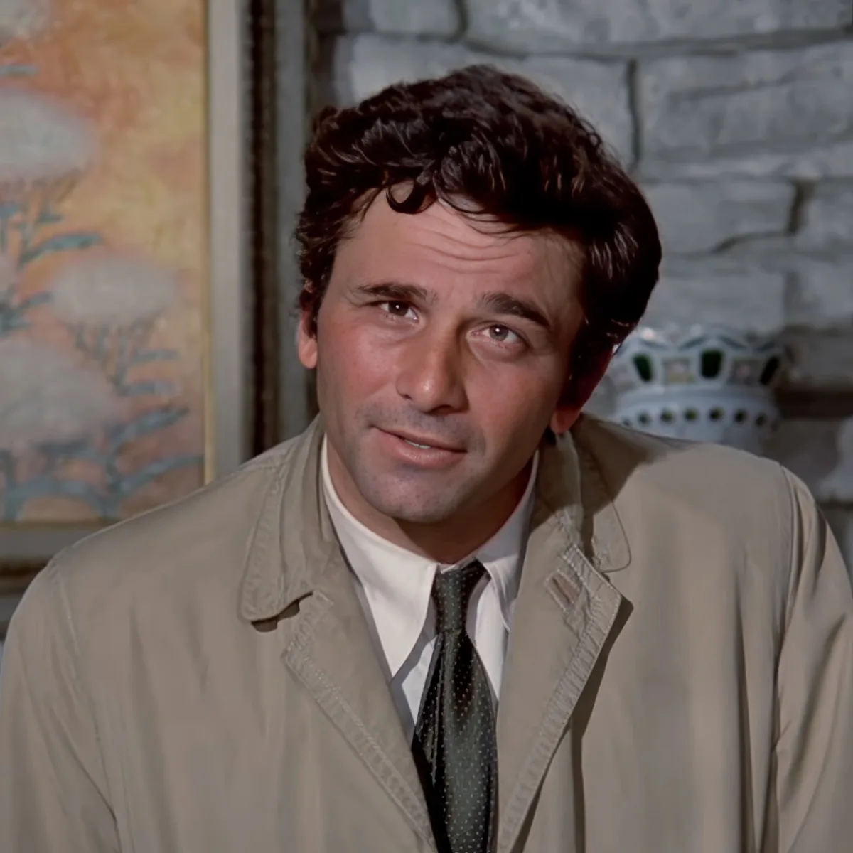 A man in a beige trench coat and white shirt with a green tie is looking to the side.