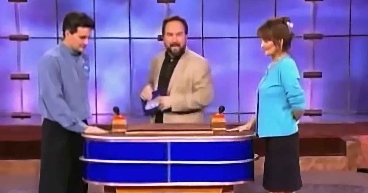 Three people stand behind a blue desk on a stage with a purple-lit background.