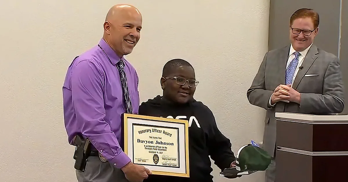 A man in a purple shirt holds a framed award for Davyon Johnson, while another man in a suit stands behind a podium.