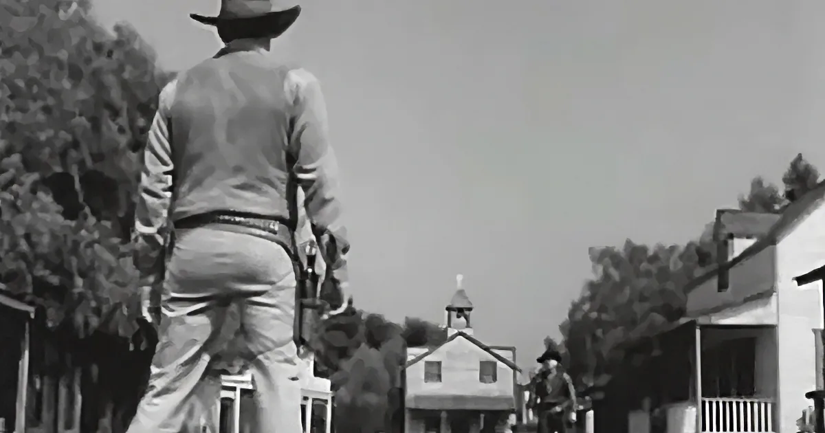 A cowboy in a hat and vest stands in a dusty town, facing away, with a church and buildings in the background.