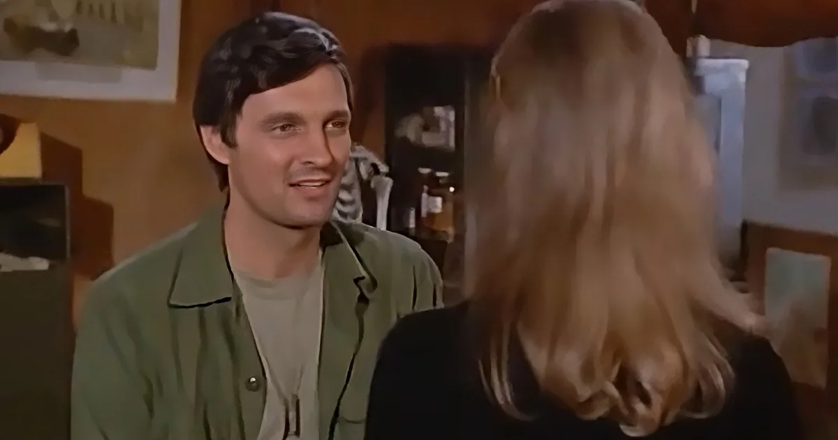 A man in a green jacket smiles at a woman with long blonde hair in a kitchen setting.
