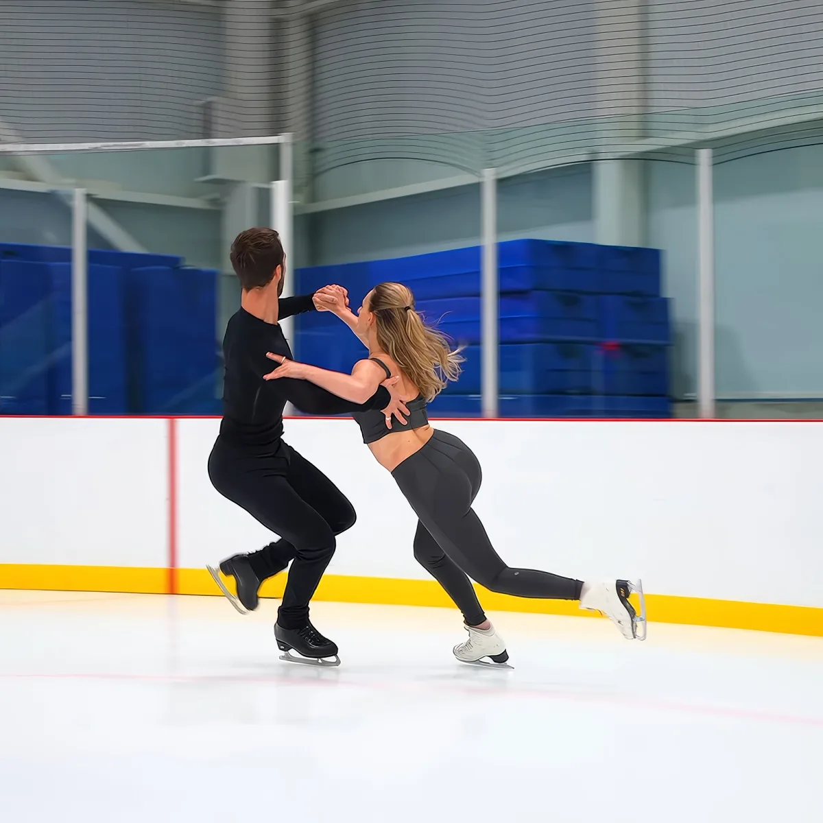 A figure skating couple performs a synchronized move on an ice rink.