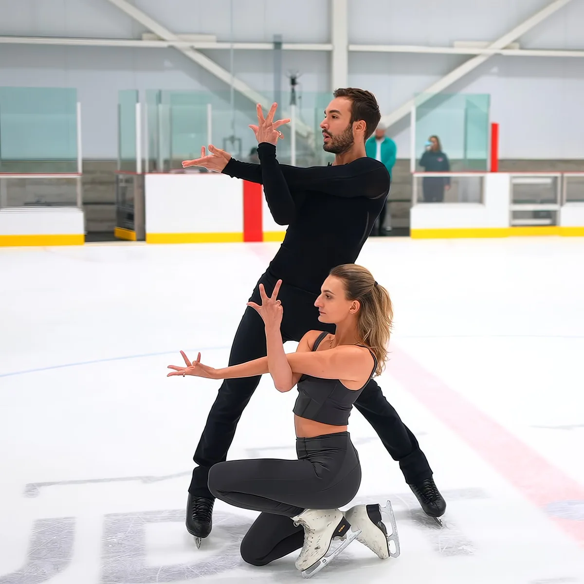 A man and woman in figure skating attire perform a synchronized pose on an ice rink.
