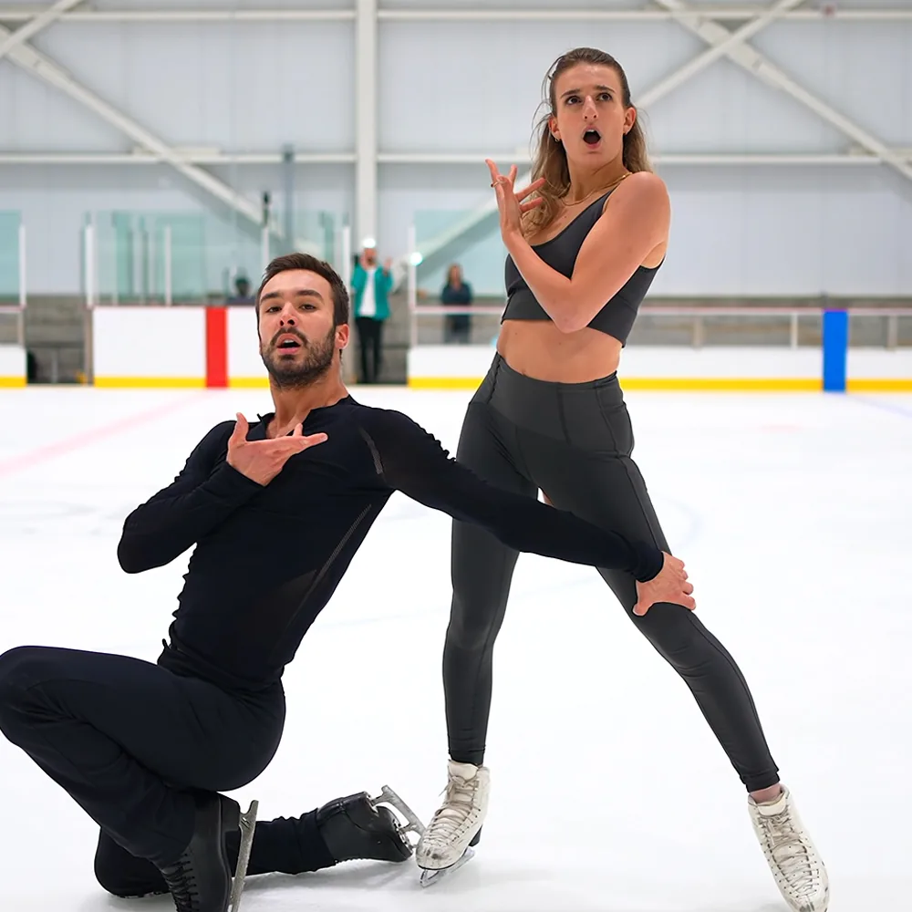 A man and woman in figure skating attire perform a dramatic pose on an ice rink.