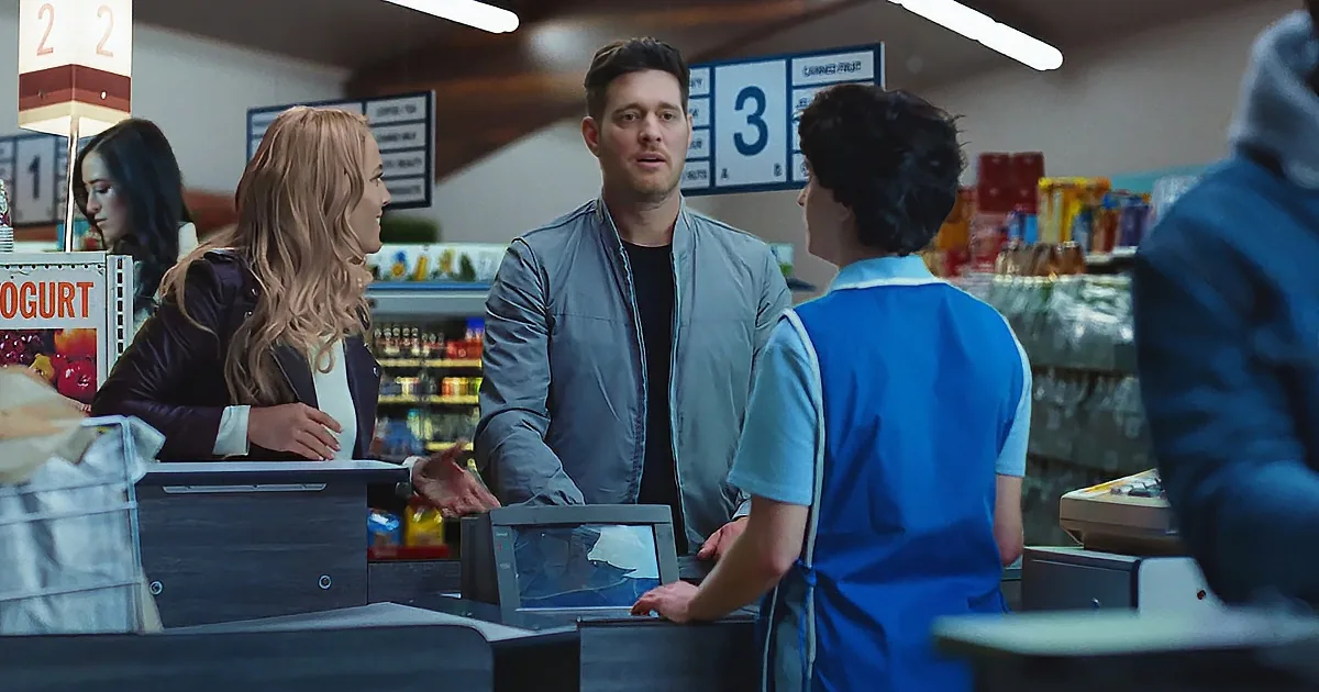 A man in a gray jacket is talking to a cashier in a blue uniform at a checkout counter.