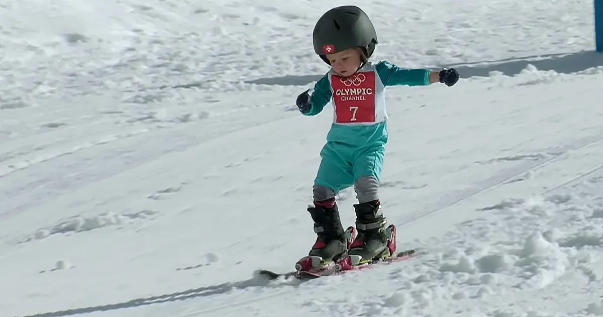 A child wearing a helmet and ski gear is skiing down a snowy slope.