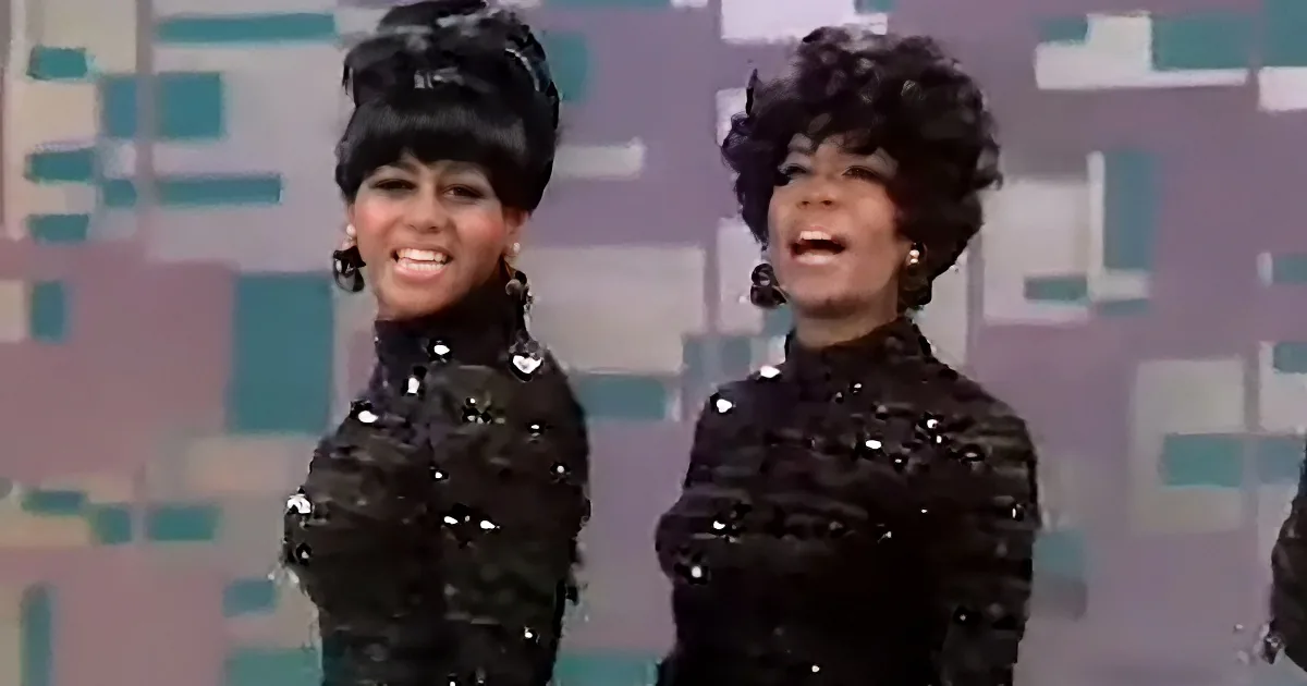 Two women in black sequined outfits with large earrings, smiling, against a colorful geometric background.