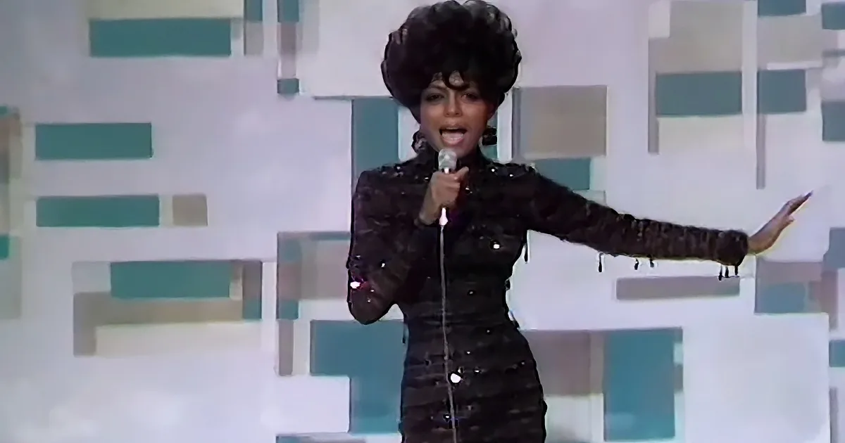 A woman in a black sequined dress sings into a microphone on stage.