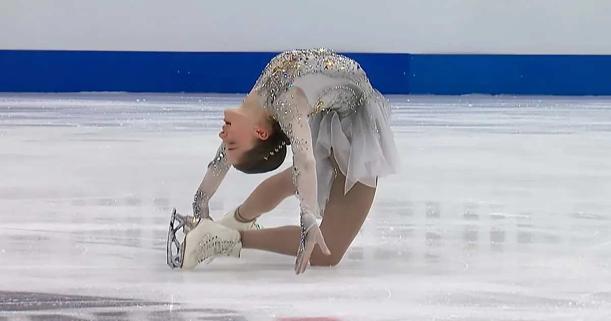 A figure skater in a white dress with sparkles performs a split on the ice.