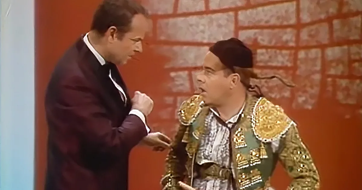 A man in a suit is pointing at another man in a bullfighter's costume, who is holding a sword.