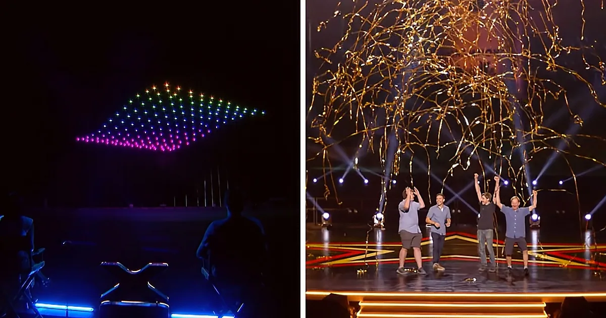 A drone formation creates a colorful pattern above a stage where four people celebrate with raised arms.