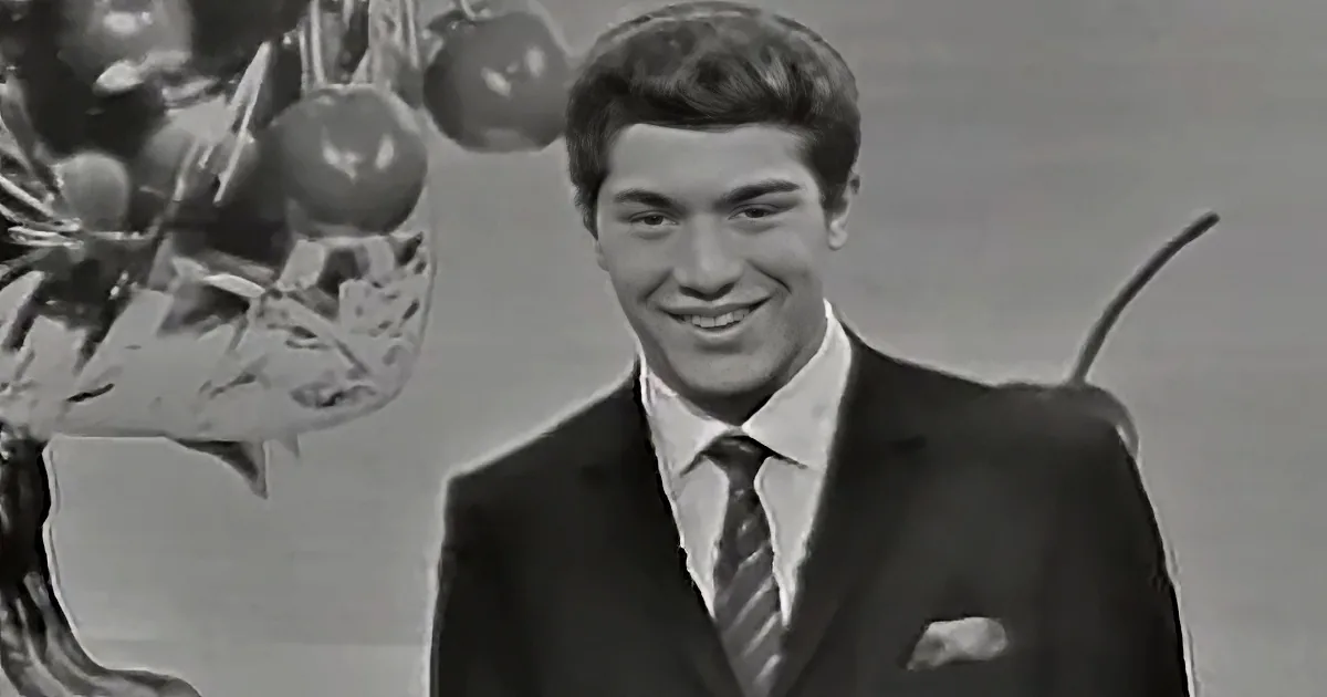 A man in a suit smiles, standing in front of a decorative tree with ornaments.