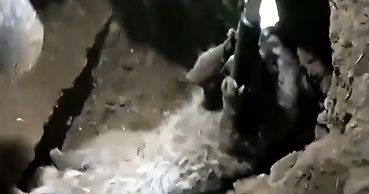 A person is climbing through a rocky cave entrance, with their hands and feet visible.