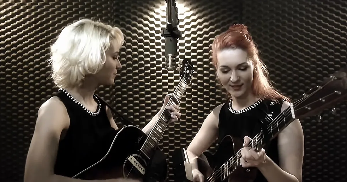 Two women in black dresses play guitars in a recording studio with acoustic foam.